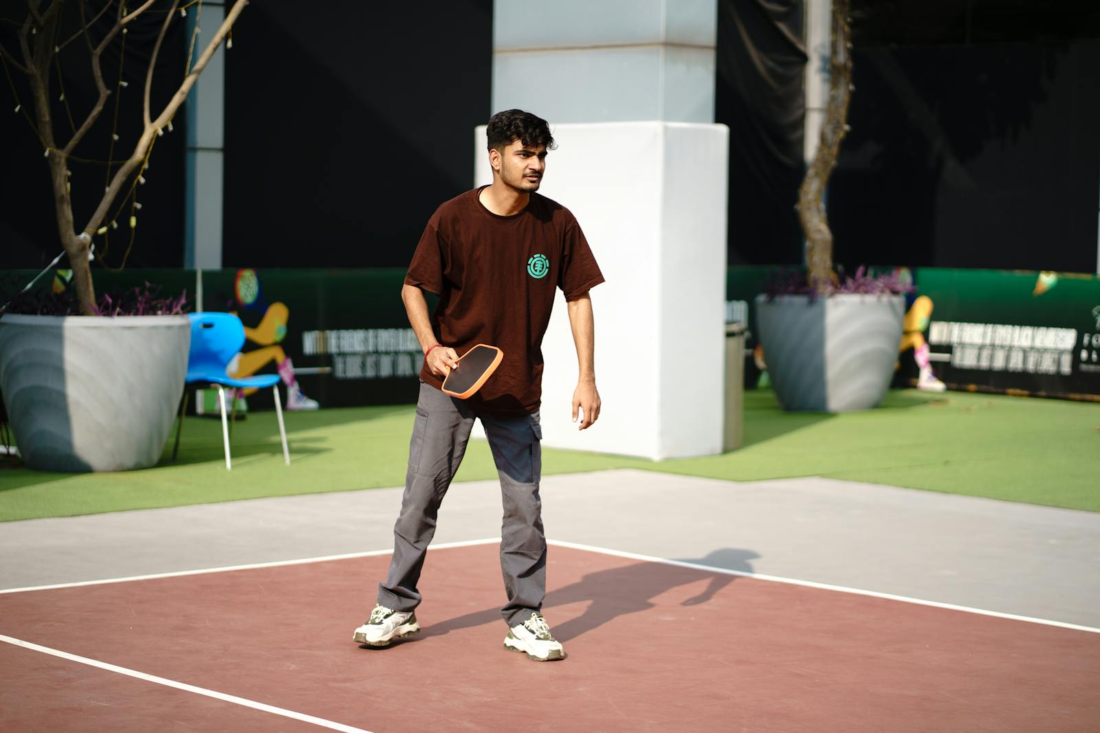En ung person spelar pickleball på en utomhusbana i stadsmiljö.