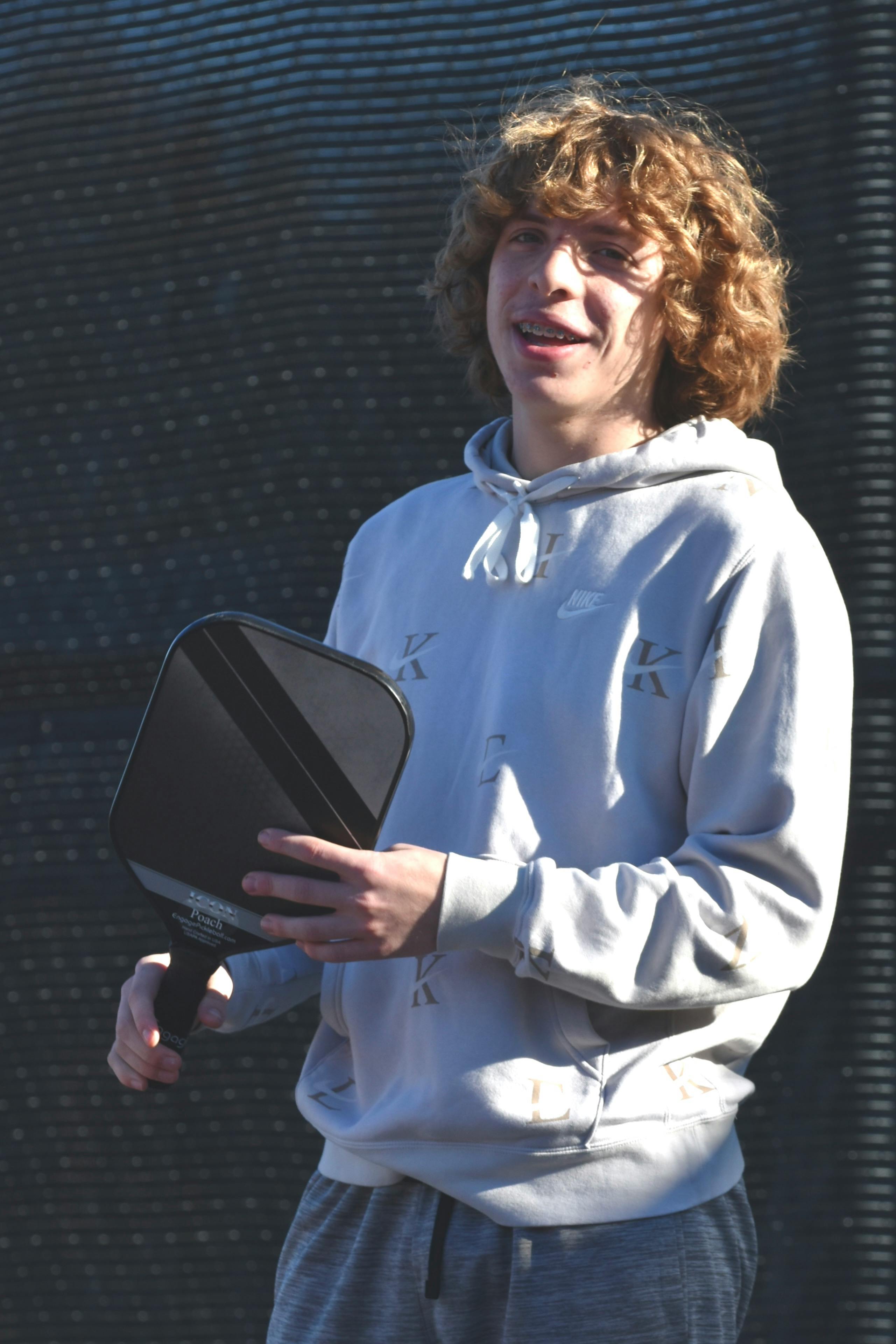 En ung person håller ett pickleballracket utomhus.